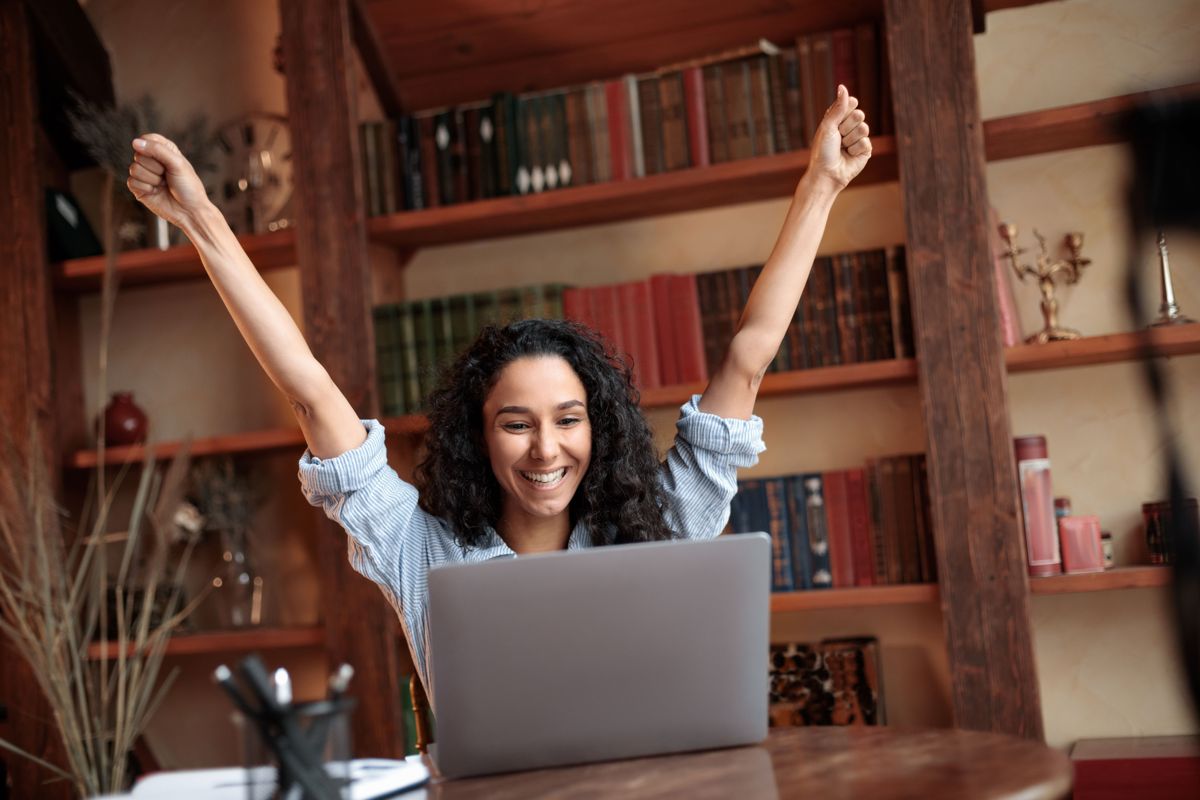 A delighted woman throwing her arms up in front of her laptop